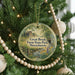 A round ornament hanging on a Christmas tree, featuring a scenic image of a farm and a stream.
