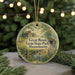 A round ornament with a painting of a farm scene hangs in front of a Christmas tree with lights.