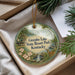 A decorative ornament with a scenic image of a lake and a cabin, surrounded by pine trees, is placed in a box with pine branches.