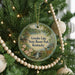 A round ornament hanging on a Christmas tree, featuring a scenic image of a lake and a deer.