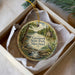 A decorative ornament in a box, featuring a scenic landscape with a waterfall and a bird, along with the text "Greenwell State Park, Maryland".