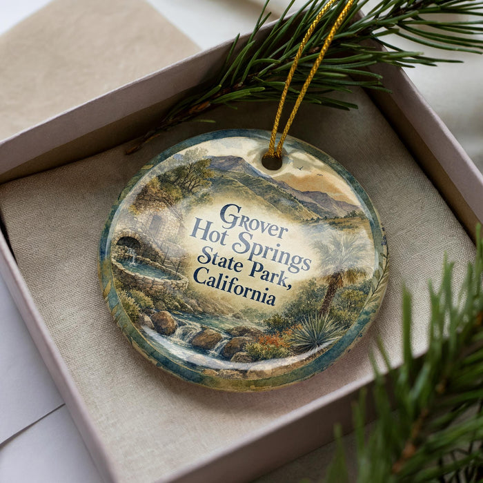 A decorative ornament in a box, featuring a scenic landscape with mountains, water, and greenery.