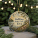 A circular ornament with a painting of a bird and a landscape, featuring the text "Gull Point State Park, Iowa" on it, hanging in front of a blurred Christmas tree with lights.