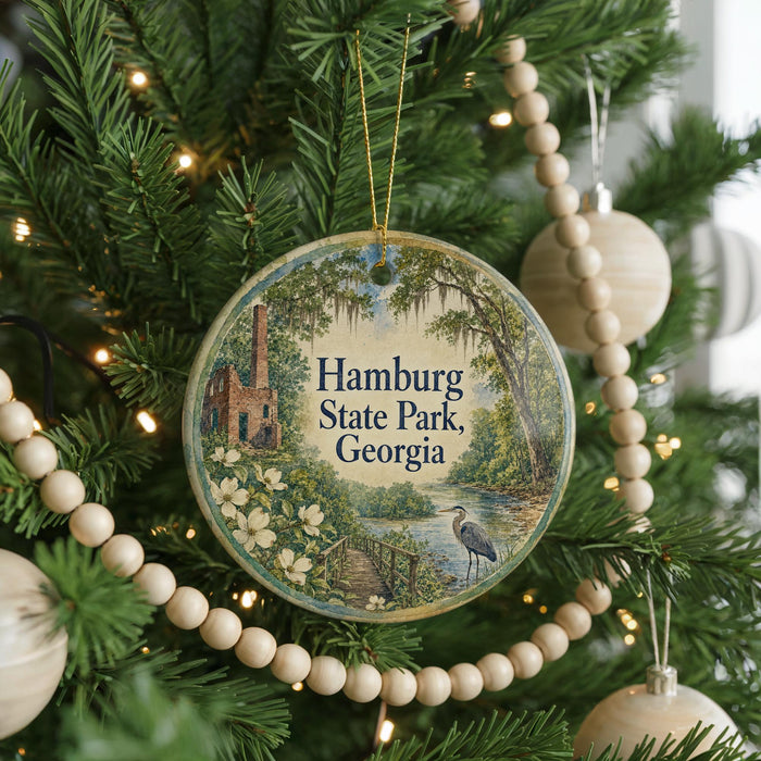 A round ornament on a Christmas tree, featuring a scenic image of Hamburg State Park in Georgia, with a bird in the foreground and a bridge in the background.
