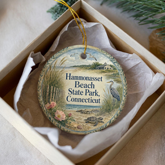 A decorative ornament in a box, featuring a beach scene with a bird, flowers, and a house.