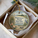 A decorative ornament in a box, featuring a beach scene with a bird, flowers, and a house.