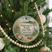 A round ornament hanging on a Christmas tree, featuring a scenic image of a beach and park with a bird in the foreground.