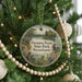 A round ornament hanging on a Christmas tree, featuring a scenic image of a pond surrounded by trees and mountains.