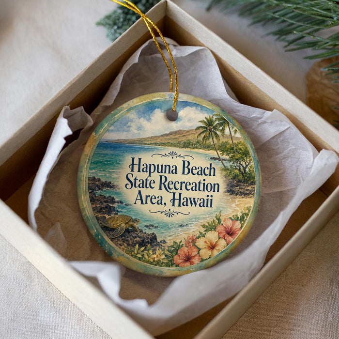 A round ornament with a beach scene and text, placed in a box with a white tissue paper lining.