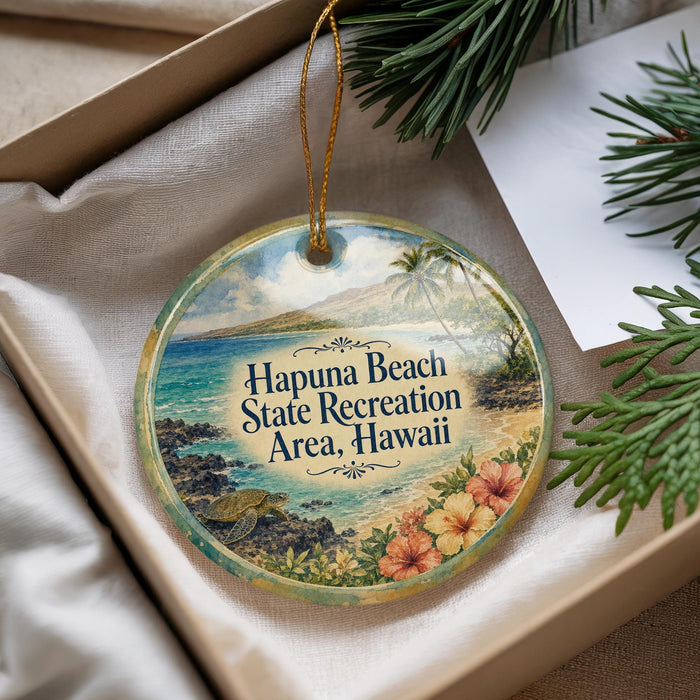 A decorative ornament with a beach scene and text, placed in a box with pine branches.