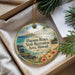 A decorative ornament with a beach scene and text, placed in a box with pine branches.
