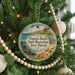 A circular ornament hanging on a Christmas tree, featuring a tropical beach scene with palm trees and a body of water.