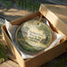 A round ornament in a wooden box, featuring a scenic image of a historic farm and park in Georgia.