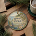 A decorative ornament with a scenic image of Harkness Memorial State Park, Connecticut, is displayed on a wooden surface alongside a cup of coffee and some pine branches.