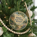 A round ornament hanging on a Christmas tree, featuring a scenic landscape with a lake and mountains.