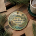 A round ornament with a scenic image of a tropical landscape, featuring a house, palm trees, and mountains, hangs on a wooden surface.