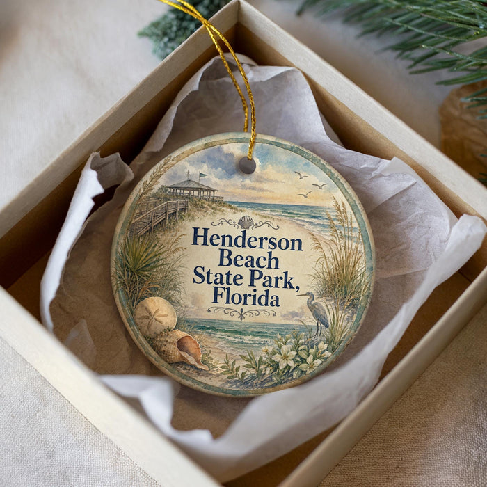 A round ornament with a beach scene and a bird is displayed in a box.