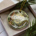 A decorative ornament in a box, featuring an illustration of Henry Cowell Redwoods State Park in California.
