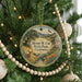 A round ornament hanging on a Christmas tree, featuring a scenic landscape with a deer, trees, and mountains.