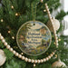 A round ornament hanging on a Christmas tree, featuring a scenic landscape with a waterfall and a cabin in the distance.