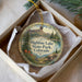 A decorative ornament in a box, featuring a scenic landscape with mountains, trees, and a lake.