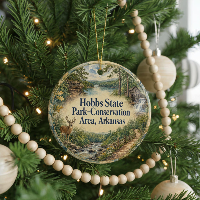 A round ornament hanging on a Christmas tree, featuring a scenic landscape with a river, trees, and a deer.