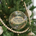 A round ornament hanging on a Christmas tree, featuring a scenic landscape with a river, trees, and a deer.