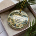 A round ornament with a scenic landscape of Holbrook Island, Maine, featuring a bird, flowers, and a path.