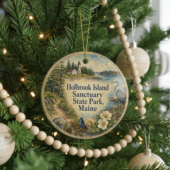 A round ornament hanging on a Christmas tree, featuring a scenic image of Holbrook Island, Maine, with a lighthouse and a bird in the foreground.