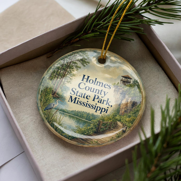 A decorative ornament in a box, featuring a scenic landscape with a lake, trees, and a bird, along with the text "Holmes County State Park, Mississippi".