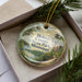 A decorative ornament in a box, featuring a scenic landscape with a lake, trees, and a bird, along with the text "Holmes County State Park, Mississippi".
