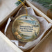 A decorative ornament in a white box, featuring a beach scene with a lighthouse, seagulls, and seashells.