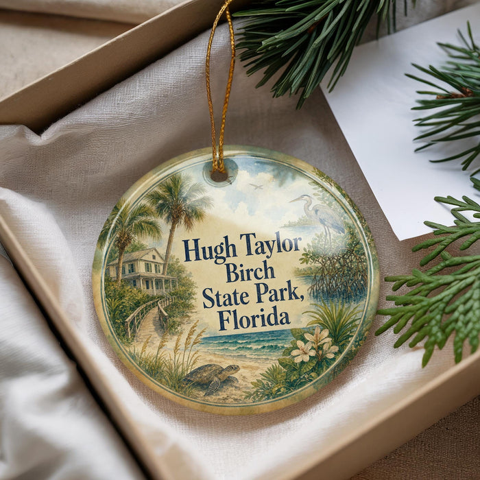 A decorative ornament with a tropical beach scene, featuring palm trees, a house, and a bird, is displayed in a box with pine branches.