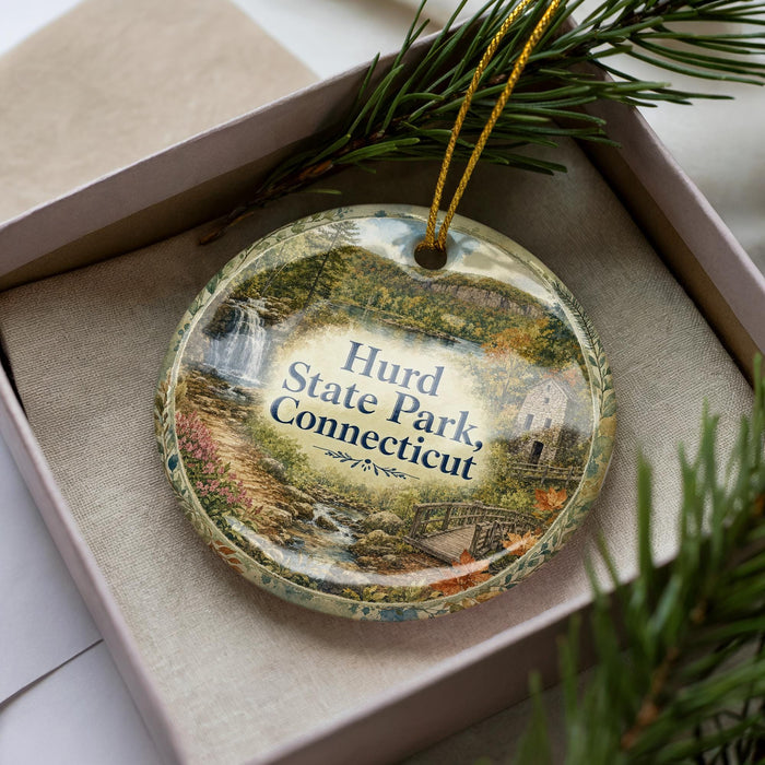A decorative ornament with a scenic image of Hurd State Park in Connecticut, displayed in a box with pine branches.