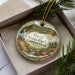 A decorative ornament with a scenic image of Hurd State Park in Connecticut, displayed in a box with pine branches.