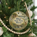A round ornament hanging on a Christmas tree, featuring a scenic landscape with a bridge and deer.