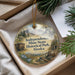 A decorative ornament with a scenic landscape and text, placed in a box with pine branches.