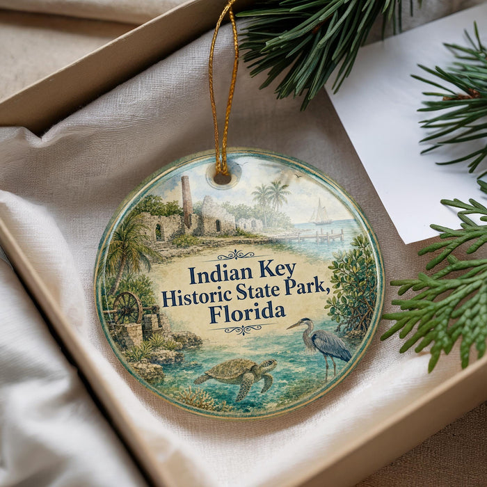 A decorative ornament with a tropical scene, featuring palm trees, a bird, and a body of water, is displayed in a box with pine branches.