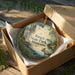 A decorative ornament in a wooden box, featuring a moose and a scenic landscape, with the text "Itasca State Park, Minnesota" printed on it.