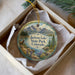 A decorative ornament in a box, featuring a scenic landscape with mountains, a lake, and a deer.