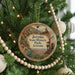 A circular ornament hanging on a Christmas tree, featuring an illustration of a desert landscape with a building and mountains in the background.