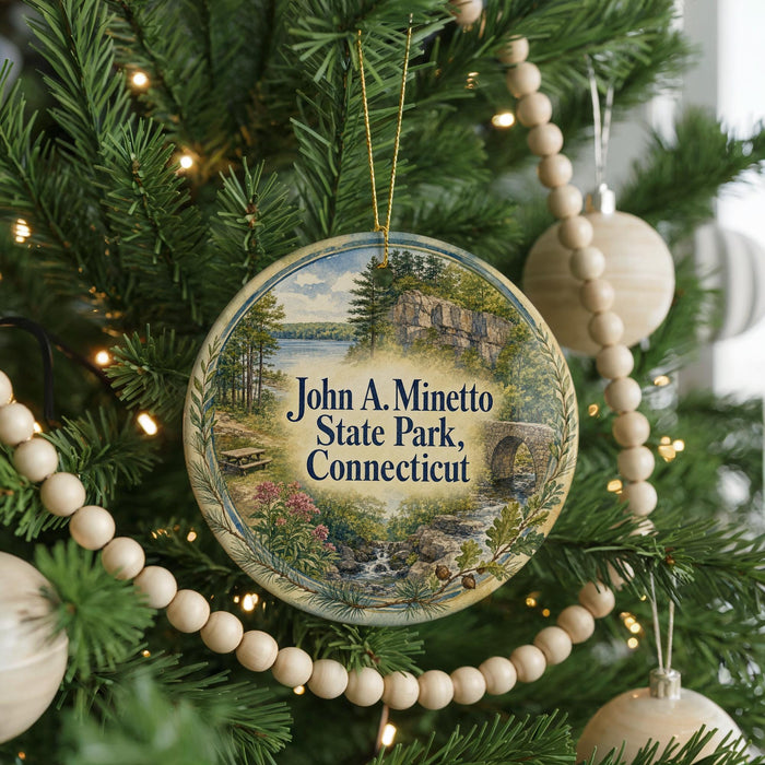 A round ornament on a Christmas tree, featuring a scenic landscape with a river, trees, and a bridge.