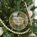 A round ornament on a Christmas tree, featuring a scenic landscape with a river, trees, and a bridge.