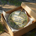 A decorative ornament in a brown box, featuring a scenic landscape with a river and trees, with the text "John A. Minetto State Park Connecticut" printed on it.