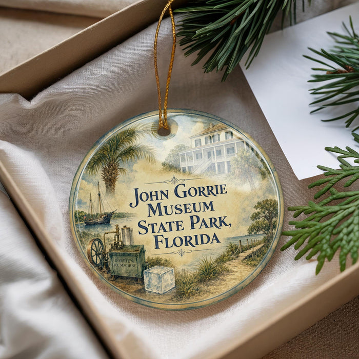 A decorative ornament with a picture of a building and palm trees, hanging from a string, placed inside a box with pine branches.