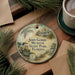A round ornament with a painting of a building and palm trees, hanging on a wooden surface.