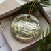 A decorative ornament in a box, featuring illustrations of a bird, a house, and trees, with text that reads "John James Audubon State Park, Kentucky".