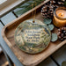 A wooden tray with a decorative ornament featuring a scenic image of John James Audubon State Park, Kentucky, along with pine cones and a lit candle.