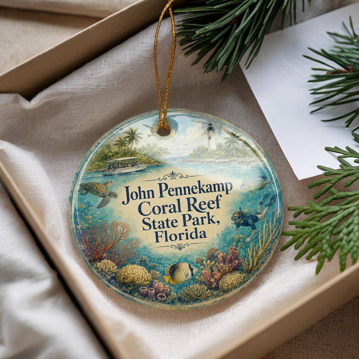 A decorative ornament with a beach scene and ocean, featuring a lighthouse and palm trees, is displayed in a box with pine branches.