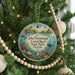 A round ornament hanging on a Christmas tree, featuring an illustration of a tropical beach scene with palm trees, a lighthouse, and a boat.